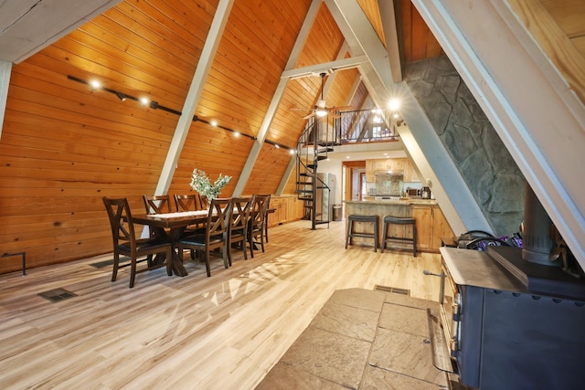 dining space featuring lofted ceiling with beams, wooden walls, wood ceiling, and light hardwood / wood-style floors