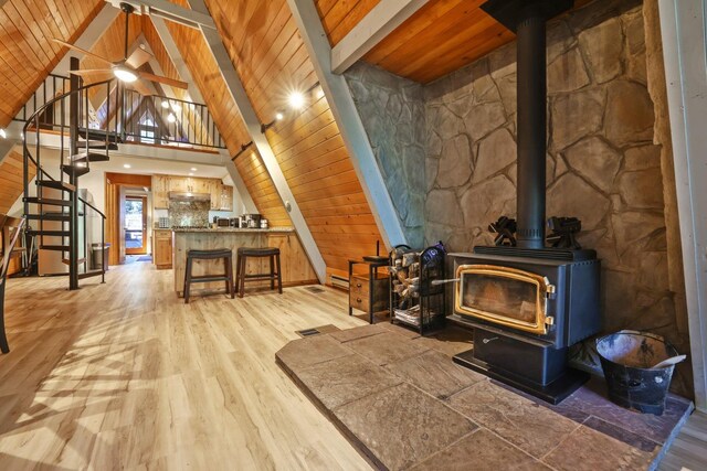 living room featuring wood ceiling, ceiling fan, beam ceiling, light hardwood / wood-style flooring, and a wood stove