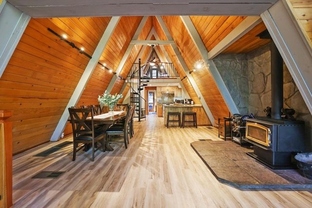 dining room with a wood stove, lofted ceiling with beams, wood ceiling, and light wood-type flooring