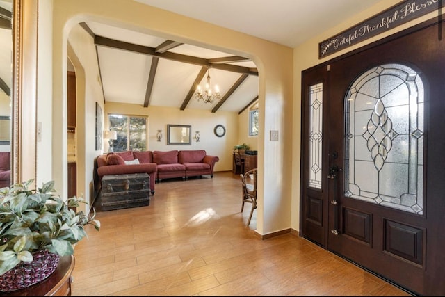 entryway featuring a chandelier, arched walkways, vaulted ceiling with beams, and plenty of natural light