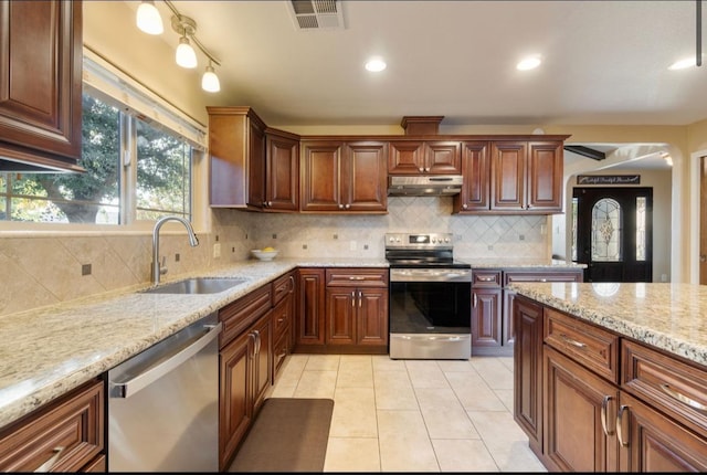 kitchen featuring light stone counters, appliances with stainless steel finishes, light tile patterned flooring, a sink, and under cabinet range hood