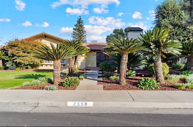 view of property hidden behind natural elements with a tile roof, a front lawn, and stucco siding