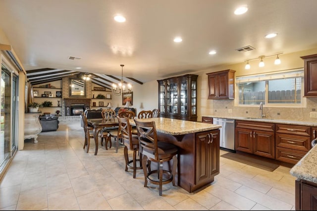 kitchen with visible vents, dishwasher, a kitchen island, hanging light fixtures, and a fireplace