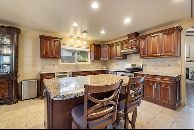 kitchen with under cabinet range hood, stainless steel appliances, a kitchen island, a sink, and visible vents