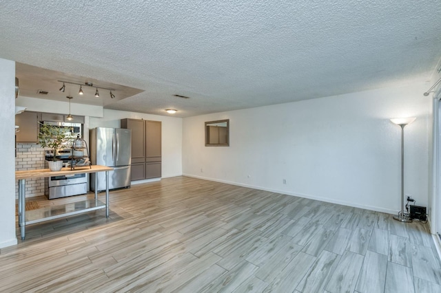 unfurnished living room featuring a textured ceiling, light wood-type flooring, and track lighting