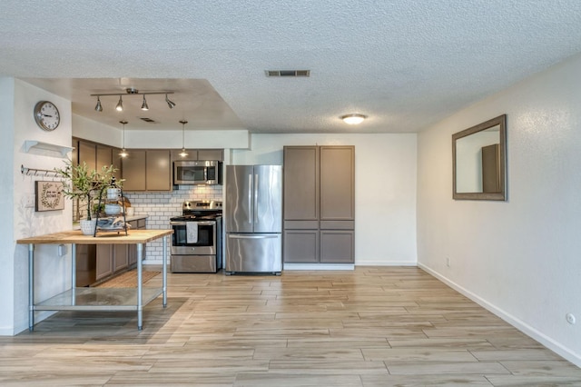 kitchen with decorative backsplash, a textured ceiling, stainless steel appliances, decorative light fixtures, and light hardwood / wood-style flooring