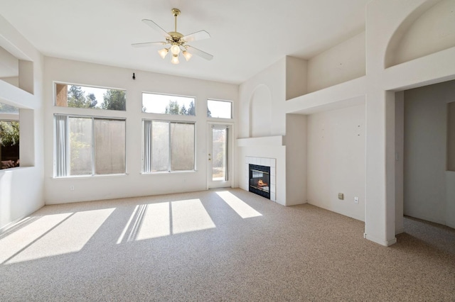 unfurnished living room with plenty of natural light, ceiling fan, light colored carpet, and a tile fireplace