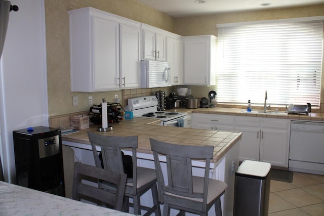 kitchen with a breakfast bar, white appliances, sink, white cabinets, and tile counters