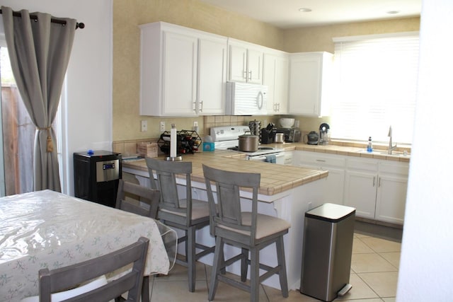 kitchen with a kitchen breakfast bar, white appliances, sink, white cabinets, and tile counters