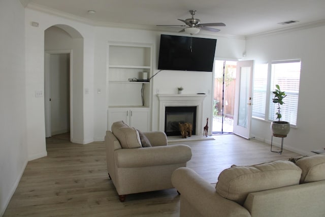 living room with light wood-type flooring, built in features, ceiling fan, and ornamental molding