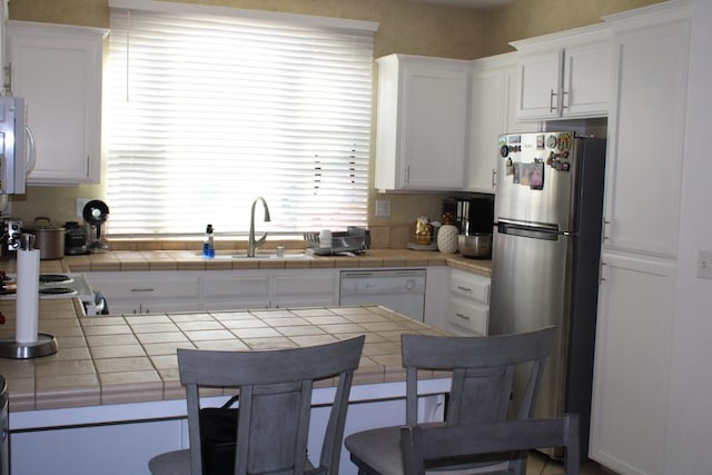 kitchen featuring a kitchen bar, stainless steel appliances, white cabinetry, and tile counters