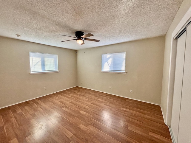 unfurnished bedroom with wood-type flooring, a textured ceiling, multiple windows, and ceiling fan