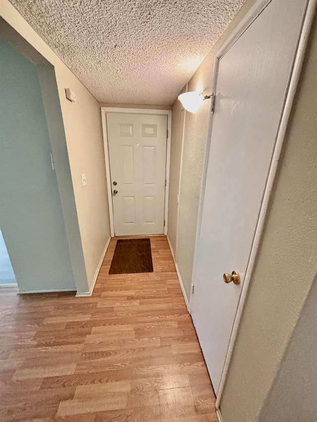 corridor with a textured ceiling and light hardwood / wood-style flooring