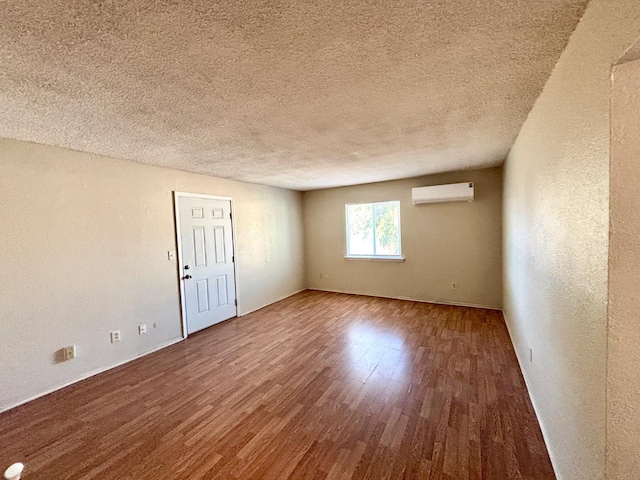 unfurnished room with wood-type flooring, a textured ceiling, and a wall unit AC