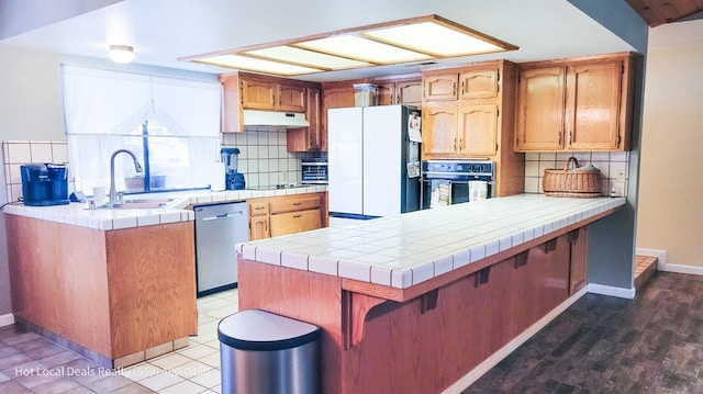 kitchen featuring tile countertops, dishwasher, white refrigerator with ice dispenser, sink, and black oven