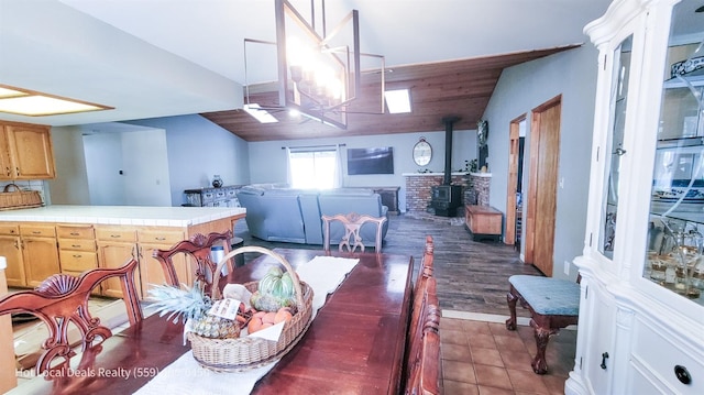 dining area with dark tile patterned flooring, vaulted ceiling, and a wood stove