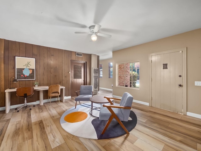 sitting room with light hardwood / wood-style floors, ceiling fan, and wooden walls