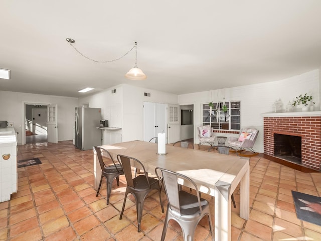 kitchen featuring stainless steel fridge, white cabinetry, a brick fireplace, and pendant lighting