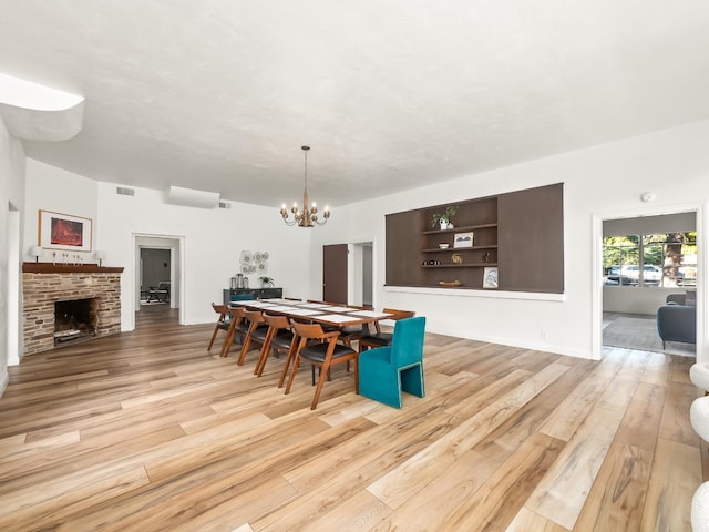 dining area featuring a fireplace, built in shelves, light hardwood / wood-style flooring, and a notable chandelier