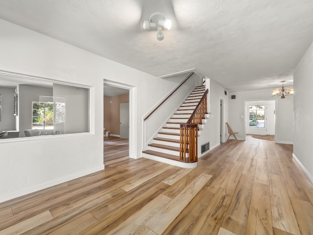 unfurnished living room with an inviting chandelier and light wood-type flooring