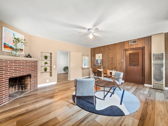 living room with a fireplace, wooden walls, light hardwood / wood-style flooring, and built in features