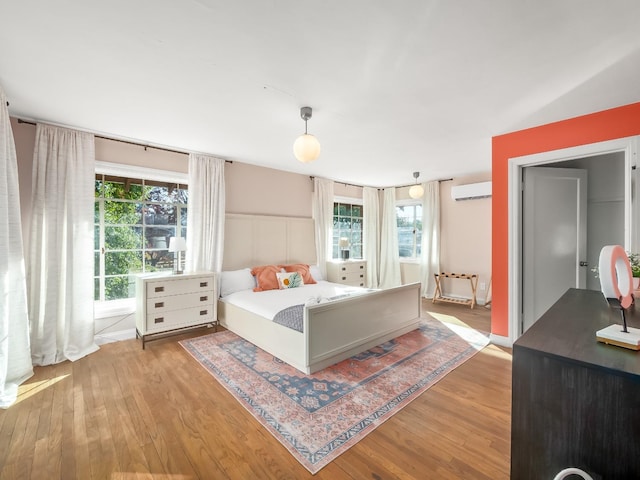 bedroom with a wall unit AC, multiple windows, and light wood-type flooring