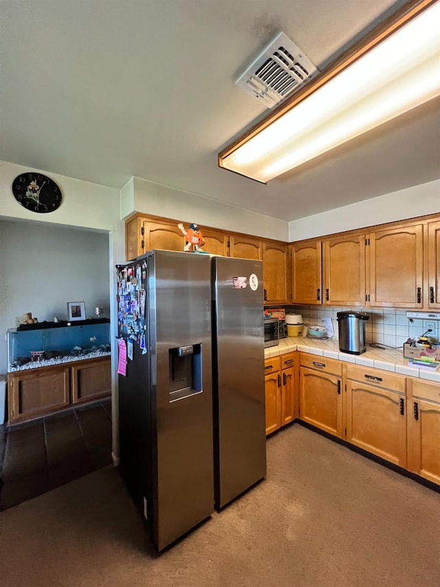 kitchen featuring tasteful backsplash, tile countertops, and stainless steel refrigerator with ice dispenser