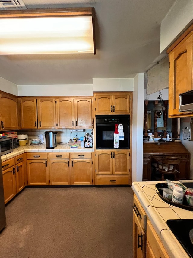 kitchen with tile counters, black oven, dark colored carpet, and tasteful backsplash