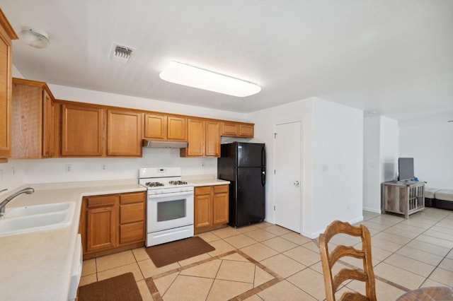 kitchen with light tile patterned flooring, black fridge, white range with gas stovetop, and sink