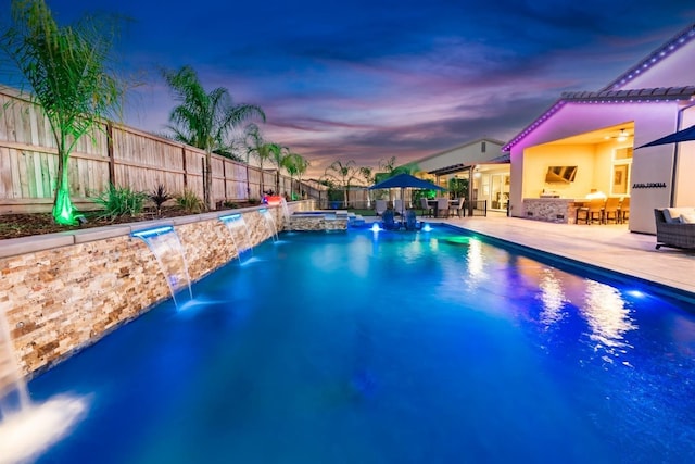 pool at dusk with a pool with connected hot tub, a fenced backyard, a patio, and outdoor dry bar