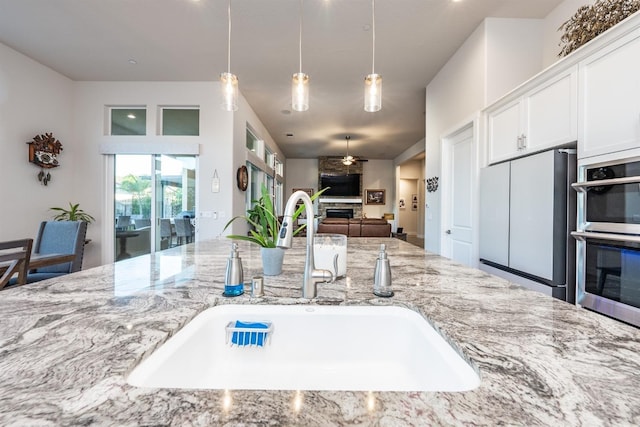 kitchen with double oven, refrigerator, a fireplace, a sink, and light stone countertops