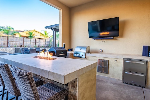 view of patio with exterior kitchen, an outdoor fire pit, fence, and grilling area