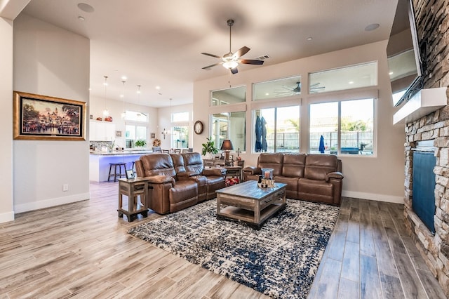 living room with visible vents, baseboards, a ceiling fan, a stone fireplace, and light wood-type flooring