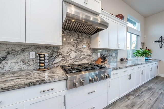 kitchen featuring under cabinet range hood, white cabinetry, decorative backsplash, light wood finished floors, and stainless steel gas stovetop