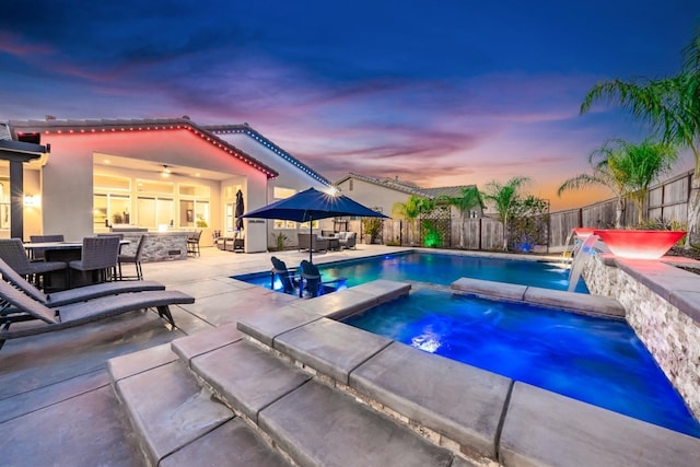 pool at dusk with a patio area, a fenced backyard, outdoor dining area, and an in ground hot tub