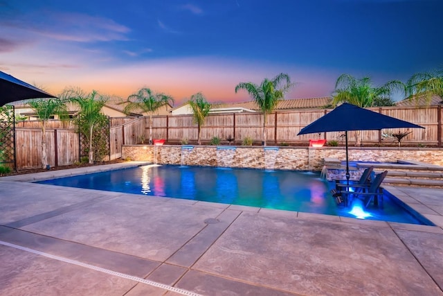 pool at dusk with a fenced backyard, a pool with connected hot tub, and a patio