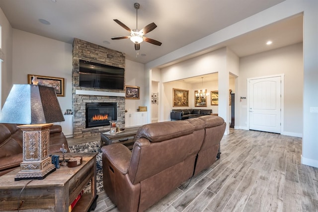 living area featuring baseboards, wood finished floors, ceiling fan with notable chandelier, a fireplace, and recessed lighting