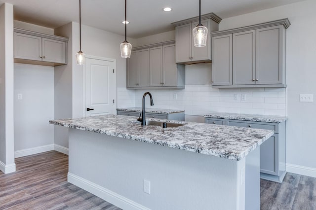 kitchen featuring tasteful backsplash, wood-type flooring, sink, hanging light fixtures, and light stone counters