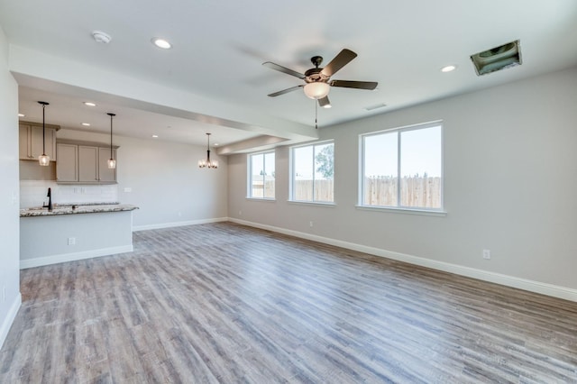 unfurnished living room featuring ceiling fan with notable chandelier, sink, and hardwood / wood-style floors