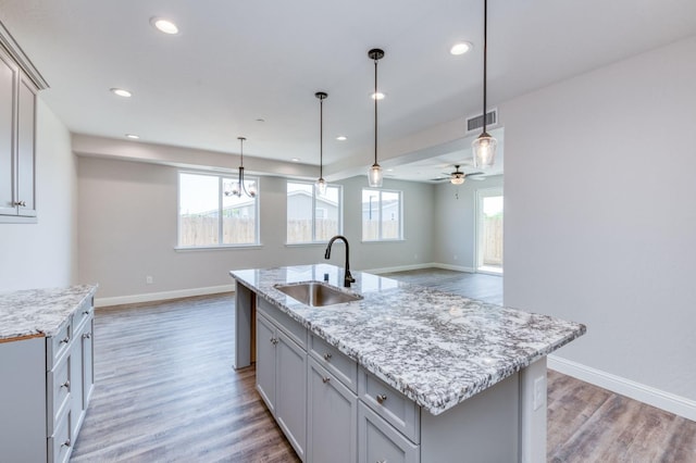 kitchen featuring gray cabinets, an island with sink, hanging light fixtures, and sink