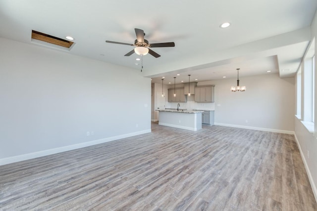 unfurnished living room featuring ceiling fan with notable chandelier, light hardwood / wood-style floors, and sink