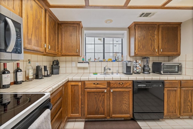 kitchen featuring black dishwasher, sink, decorative backsplash, tile counters, and light tile patterned floors