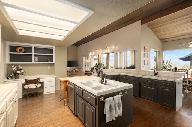 kitchen with sink, tile countertops, vaulted ceiling with beams, light hardwood / wood-style floors, and an island with sink