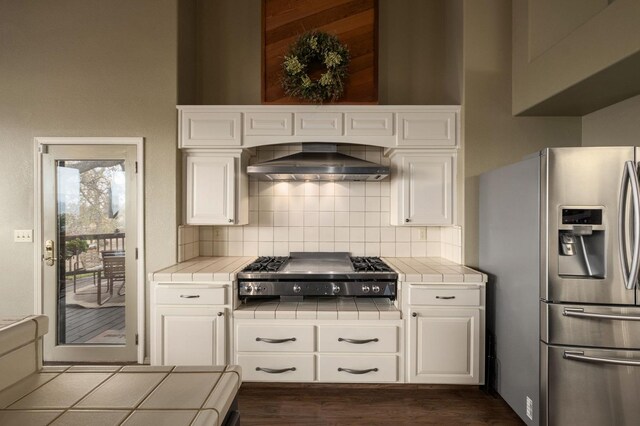 kitchen with tile counters, wall chimney range hood, and appliances with stainless steel finishes