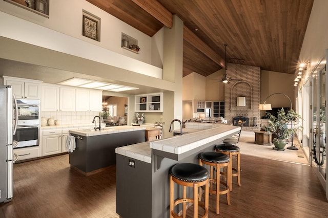 kitchen featuring tile counters, dark hardwood / wood-style floors, an island with sink, and a brick fireplace