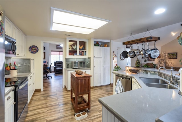 kitchen featuring white cabinets, sink, vaulted ceiling, appliances with stainless steel finishes, and light hardwood / wood-style floors