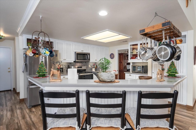 kitchen featuring stainless steel appliances, dark hardwood / wood-style flooring, kitchen peninsula, crown molding, and white cabinets