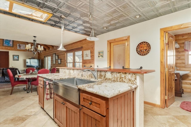 kitchen featuring an inviting chandelier, sink, stainless steel dishwasher, decorative light fixtures, and light stone counters