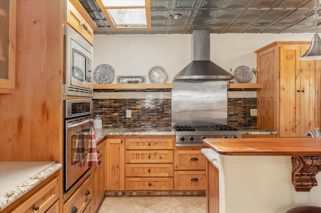 kitchen featuring tasteful backsplash, wall chimney exhaust hood, stainless steel appliances, pendant lighting, and butcher block countertops