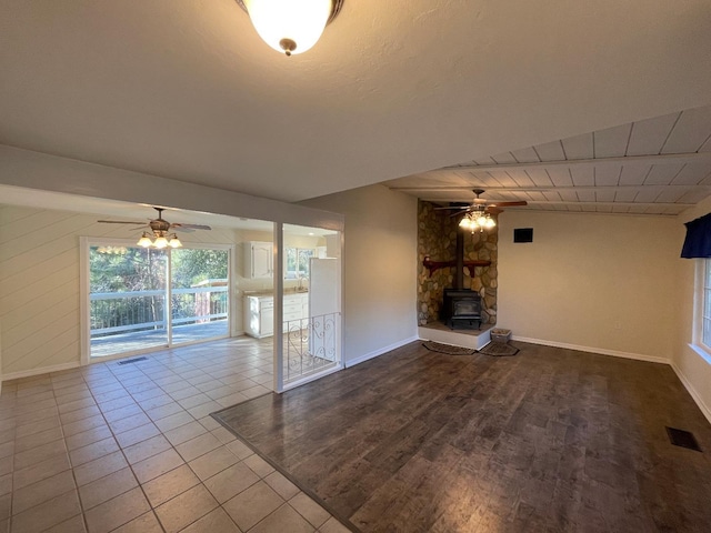 unfurnished living room featuring ceiling fan, tile patterned floors, and a wood stove